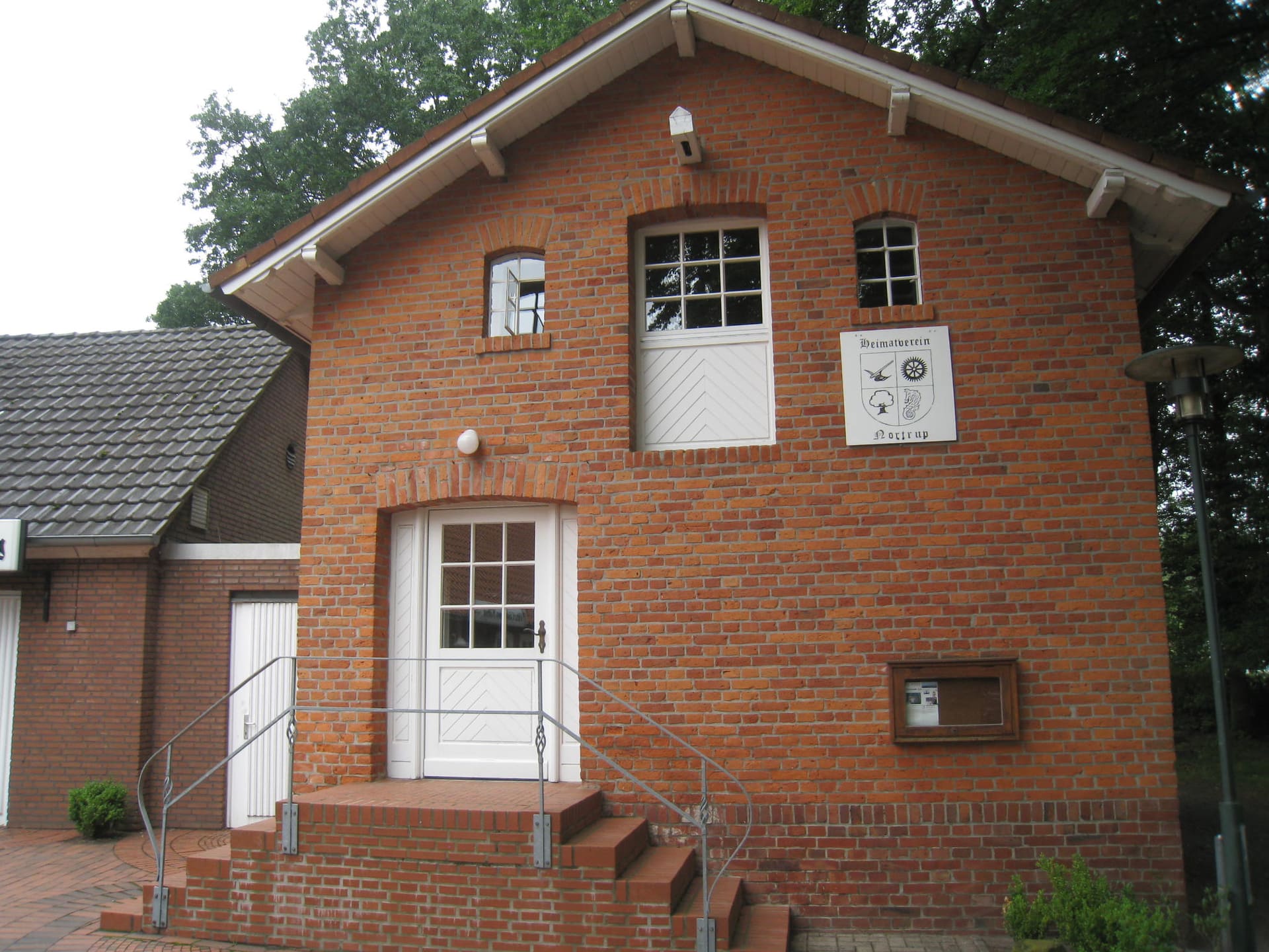 Giebel des Heimathauses aus rotem Backstein mit Treppe und weißer Tür.