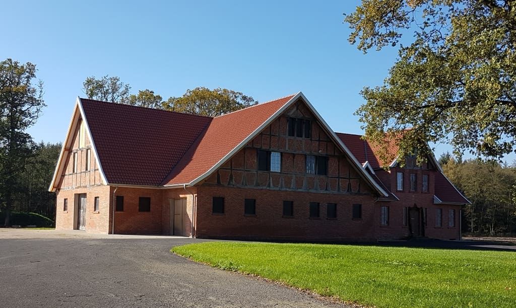 Langgestrecktes Backsteingebäude mit Fachwerkgiebeln und Rasenfläche davor.