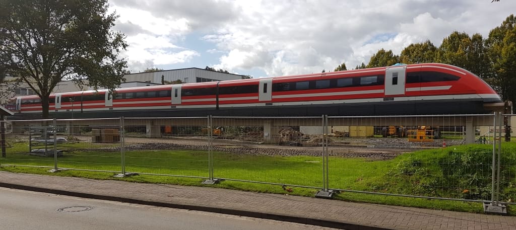 Der Transrapid auf seiner Trasse hinter einem Zaun.