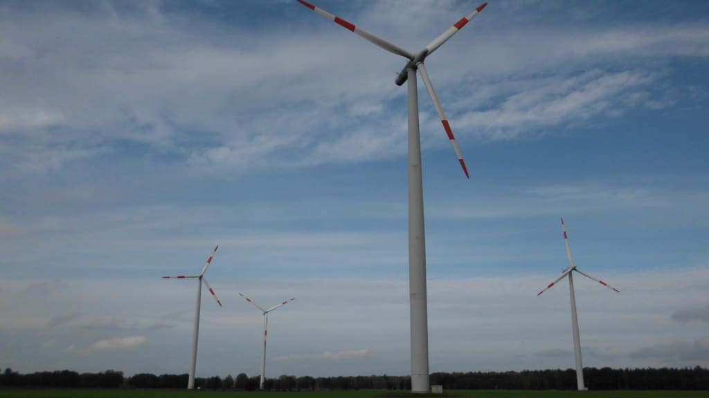 Windräder auf freiem Feld unter bewölktem Himmel.
