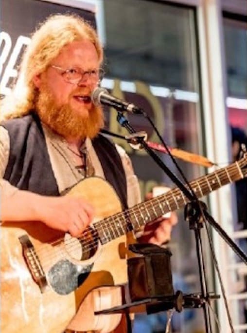 Ein Sänger mit Bart und Gitarre am Mikrofon.